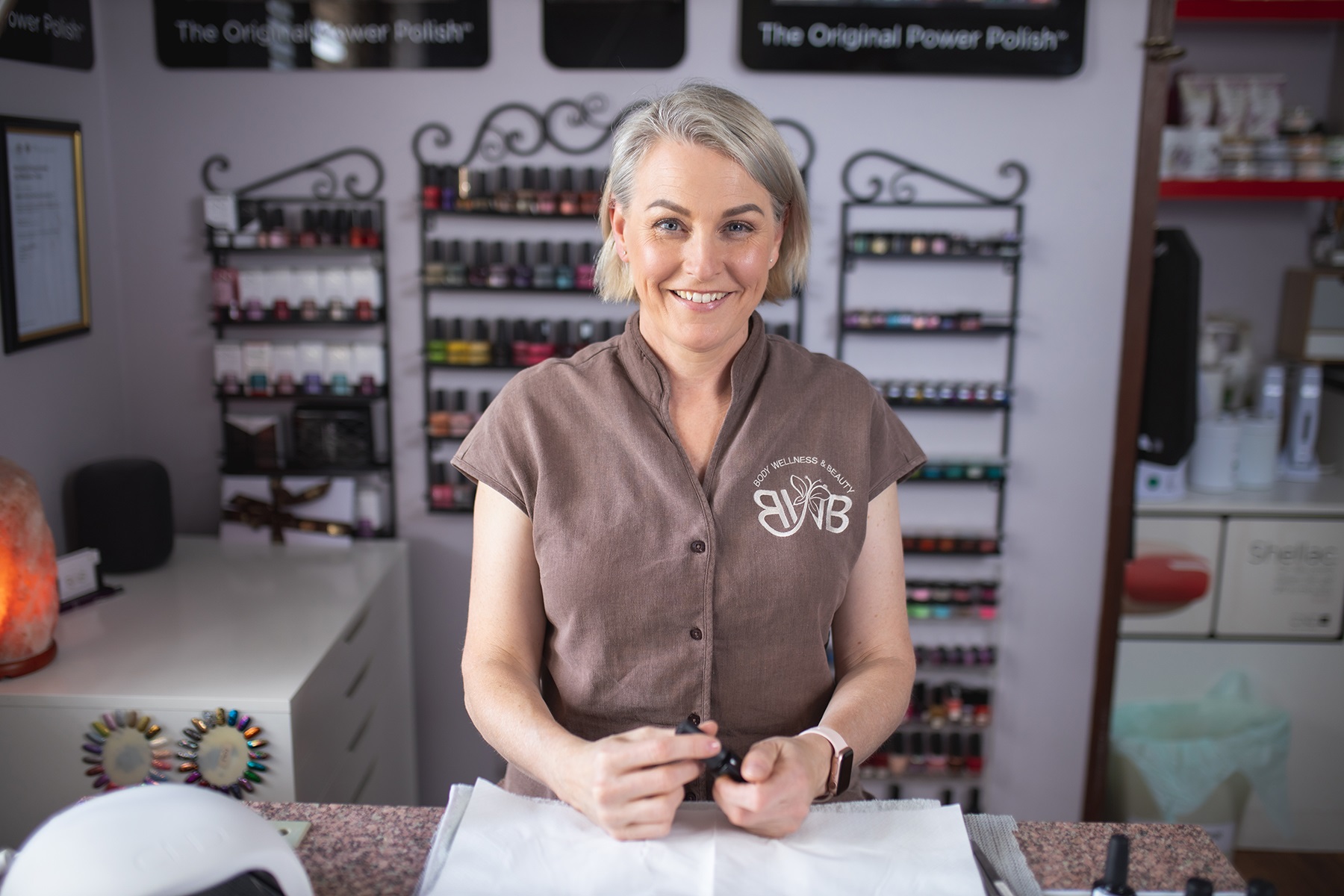 Photo of a woman in a health and beauty business. She is sitting at a table and holding a bottle of nail polish.