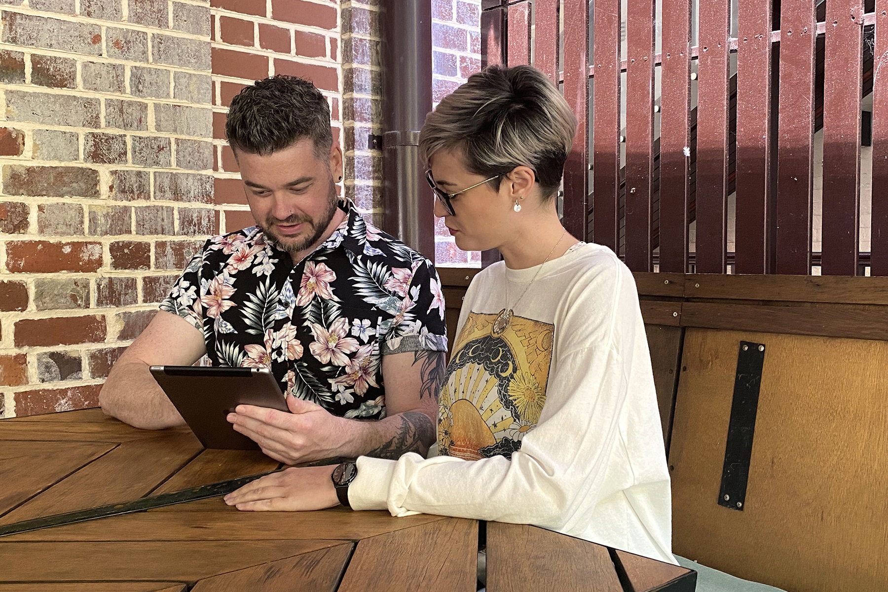 Photo of a man and woman sitting together at a table and looking at a tablet device.