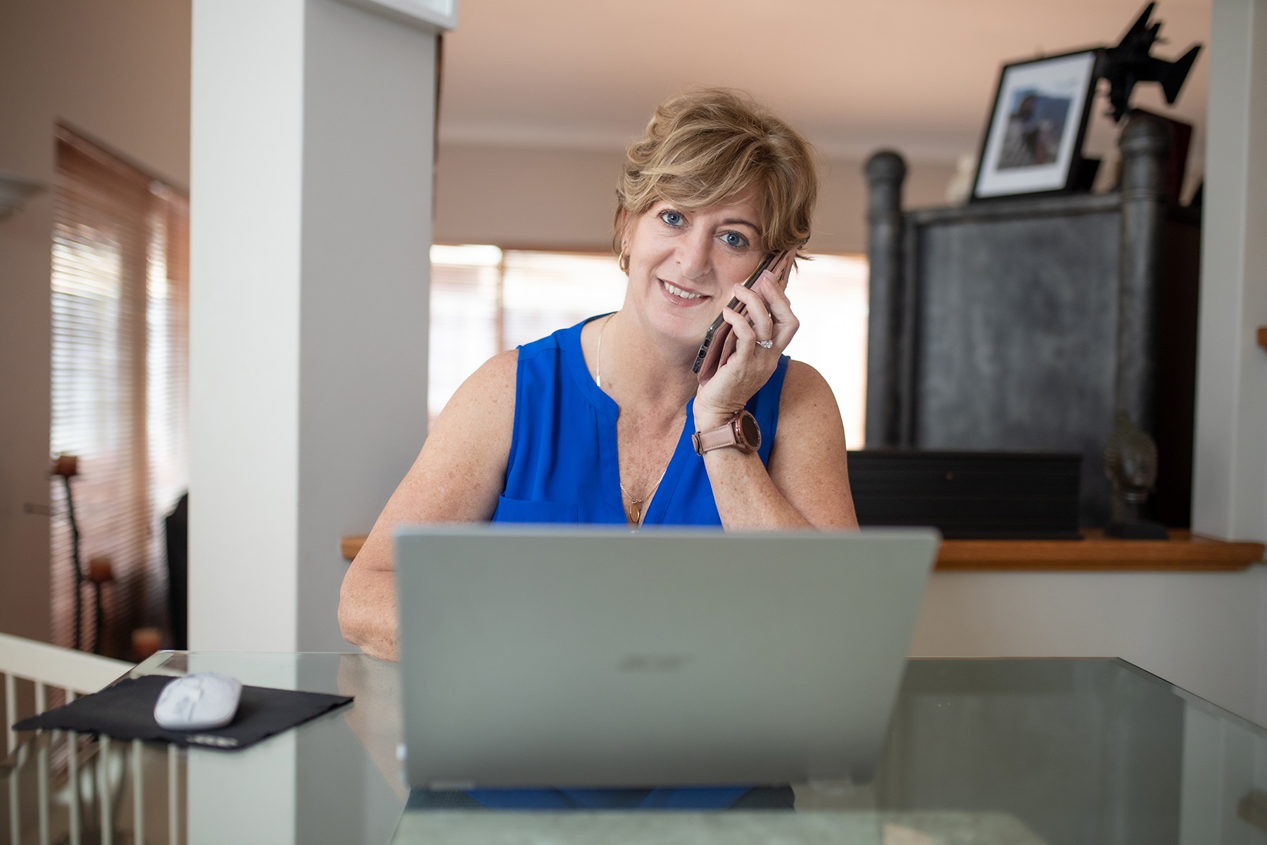 Photo of a female business owner working from home. She is sitting at a table with a laptop and speaking on the phone.